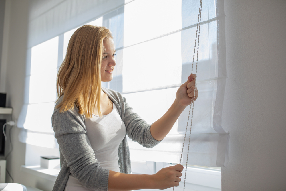 Pretty,,Young,Woman,Lowering,The,Interior,Shades/blinds,In,Her,Modern